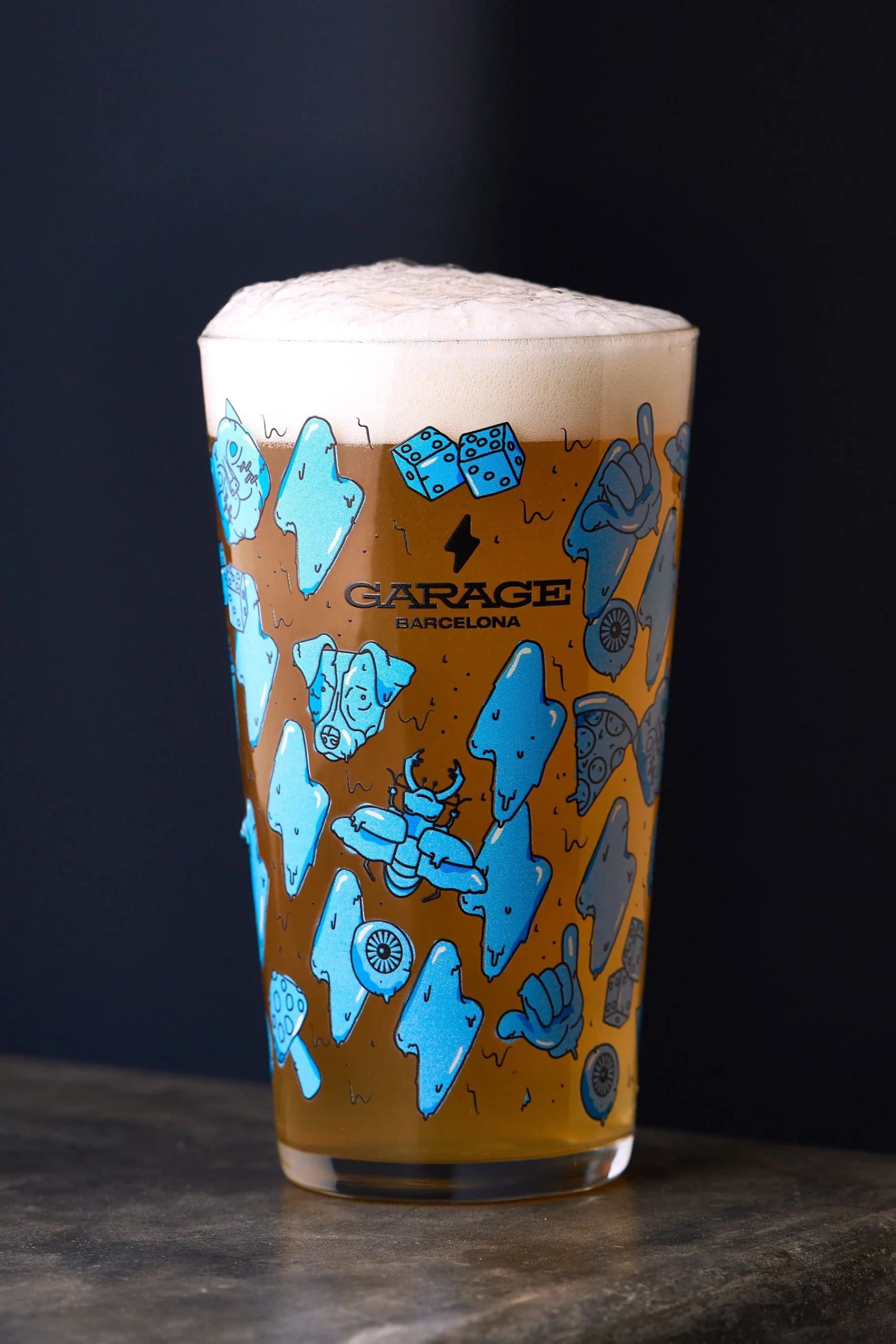 Un verre de bière dorée coiffé de mousse porte les motifs Garage Barcelona.