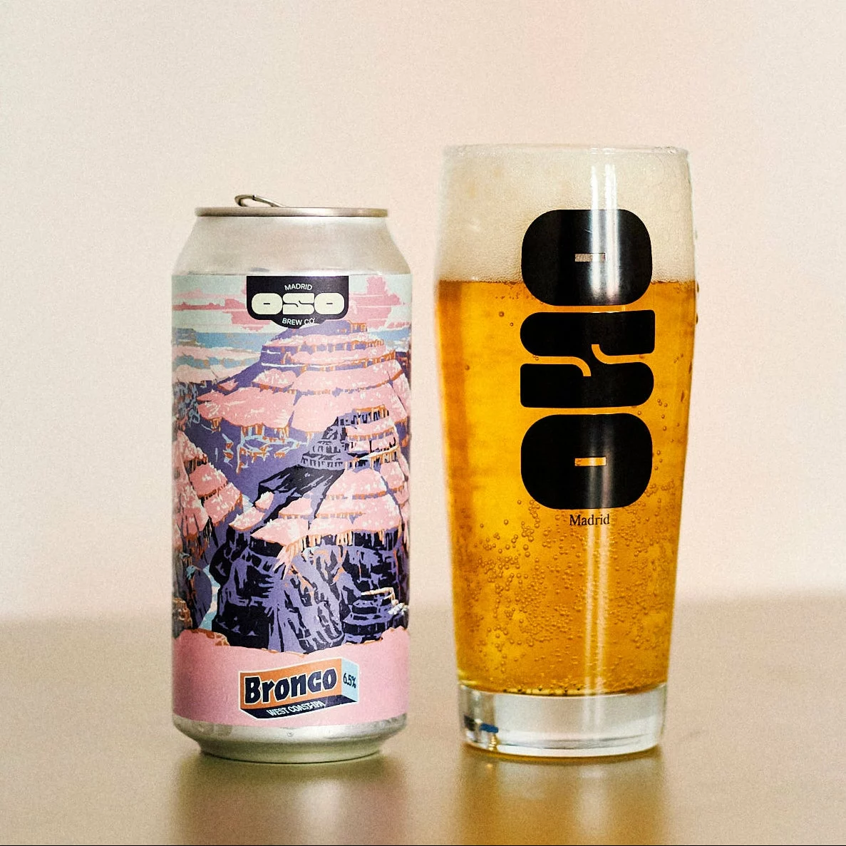 Une canette Bronco d’Oso Brew Co et un verre de bière sur fond beige.